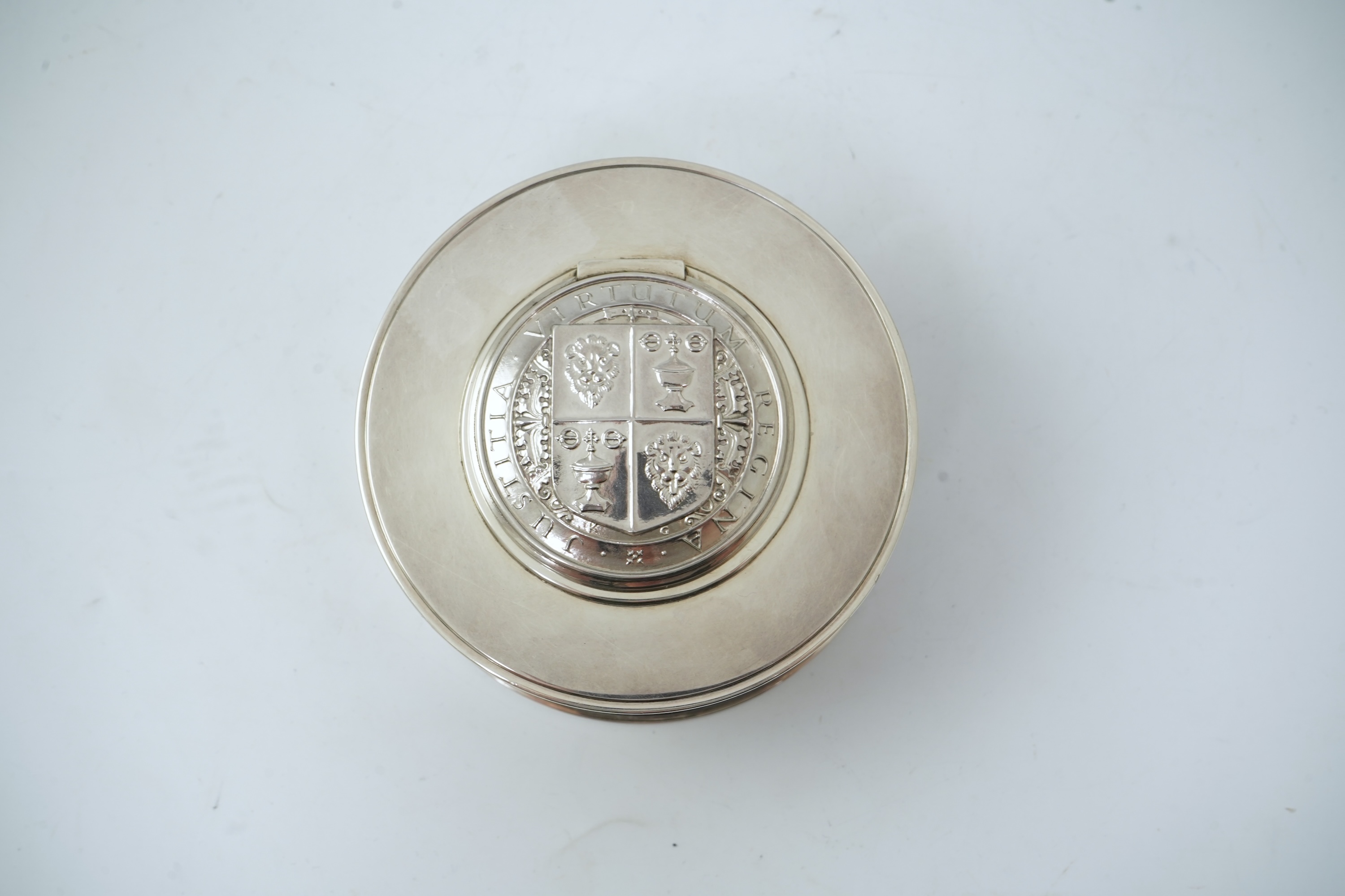 A George V silver circular inkwell, by Sebastian Garrard, commemorating the Silver Jubilee of King George V, the die stamped cover designed by George Kruger Gray featuring the Goldsmiths Company Coat of Arms
